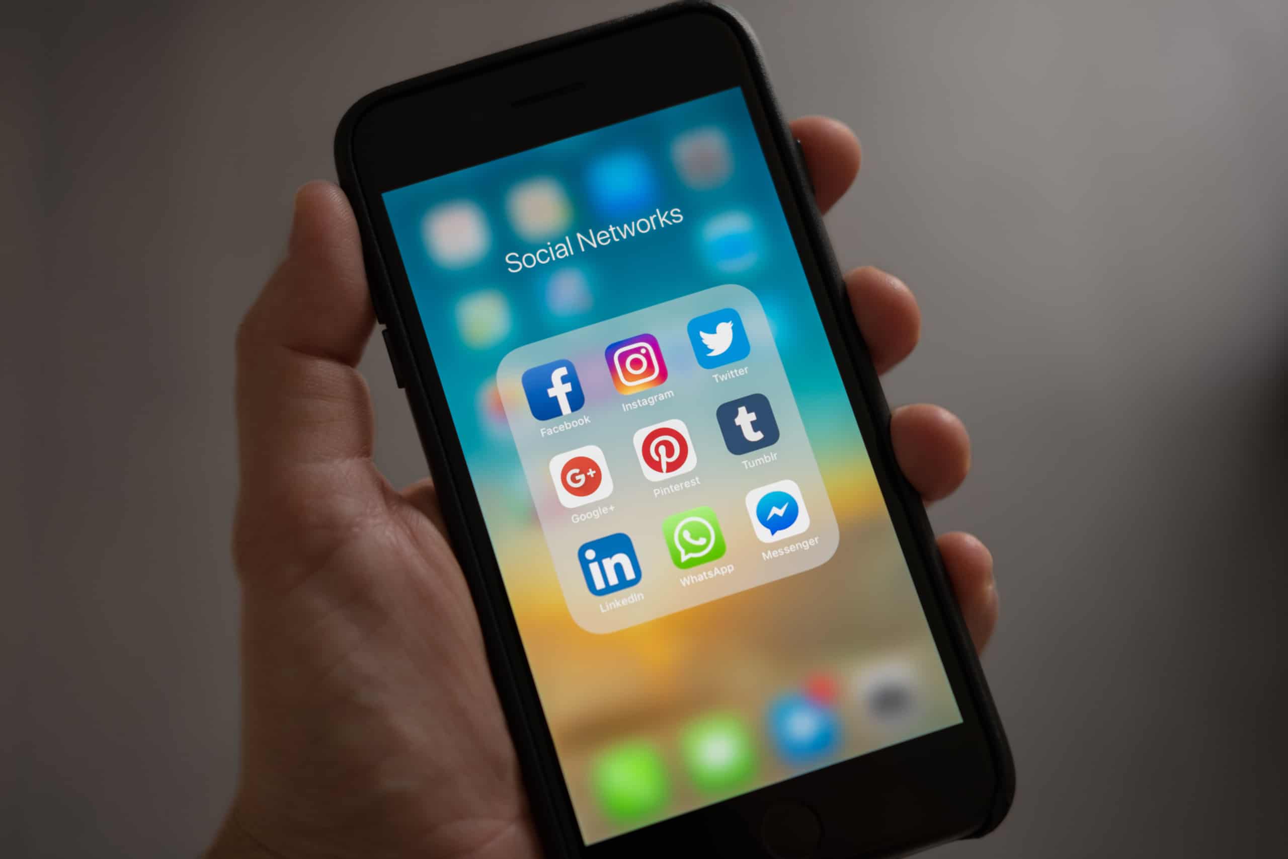 Person holding iphone showing social networks folder